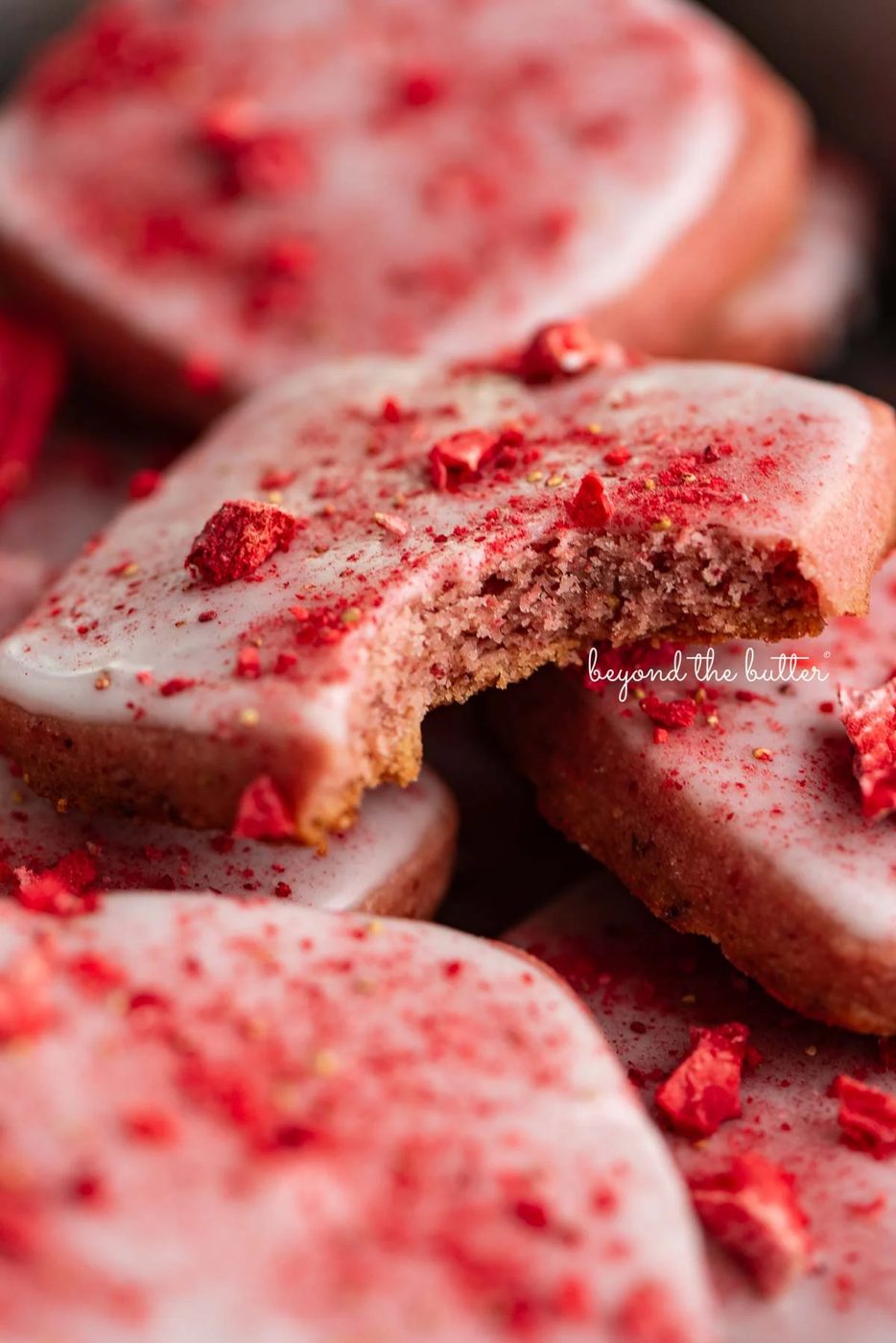 Strawberry shortbread cookies topped with glaze and freeze-dried strawberry bits randomly placed in a vintage baking tin.