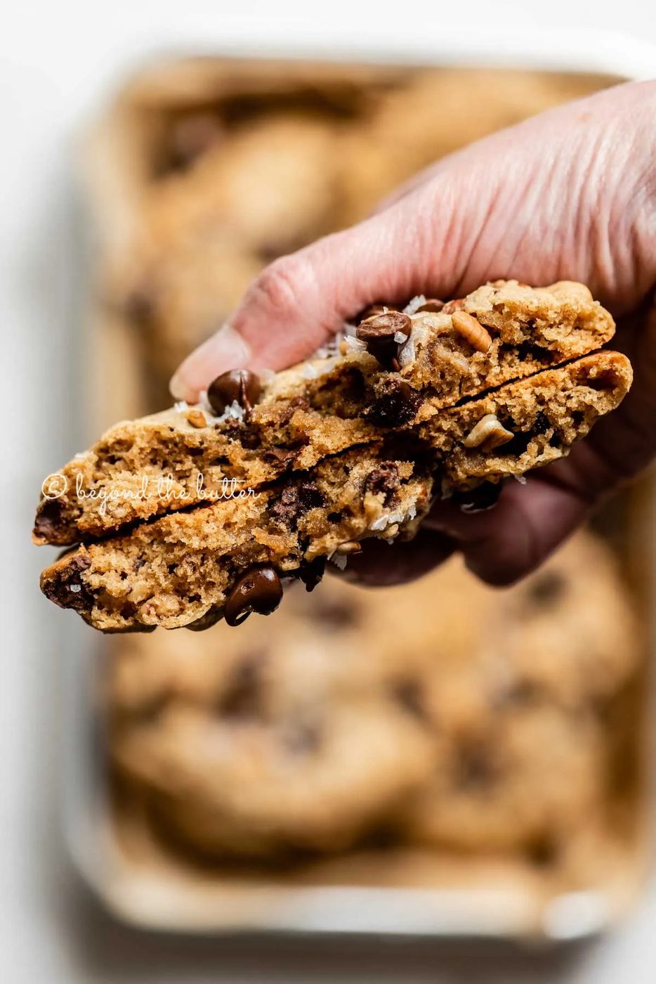 Hand holding a large almond butter chocolate chip pecan cookie that's been split in half | All images © Sovuh