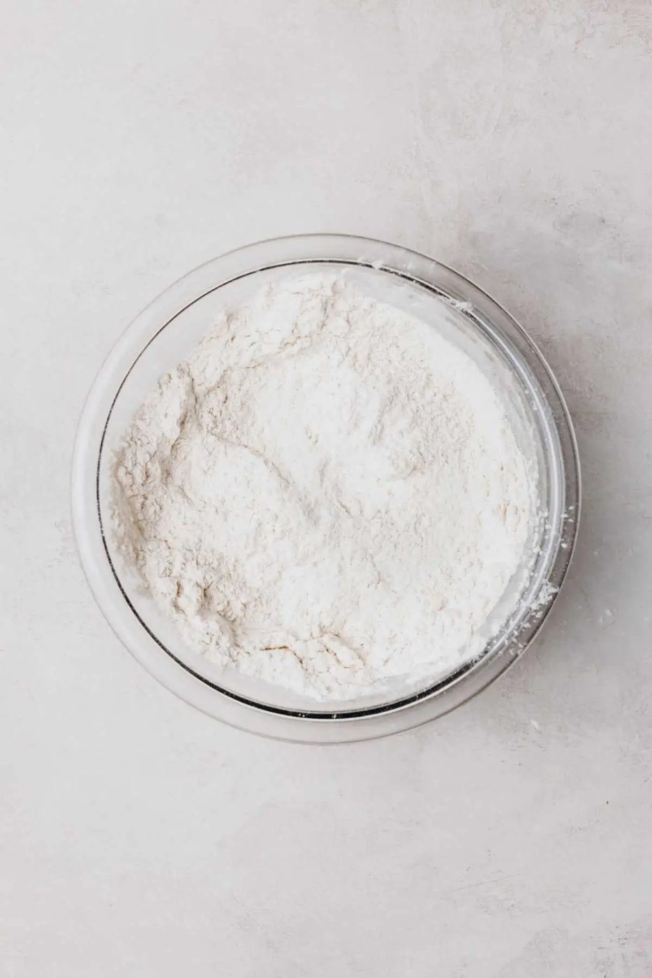 Whisked all purpose flour, baking powder, and salt in a medium size mixing bowl on a light grey background.