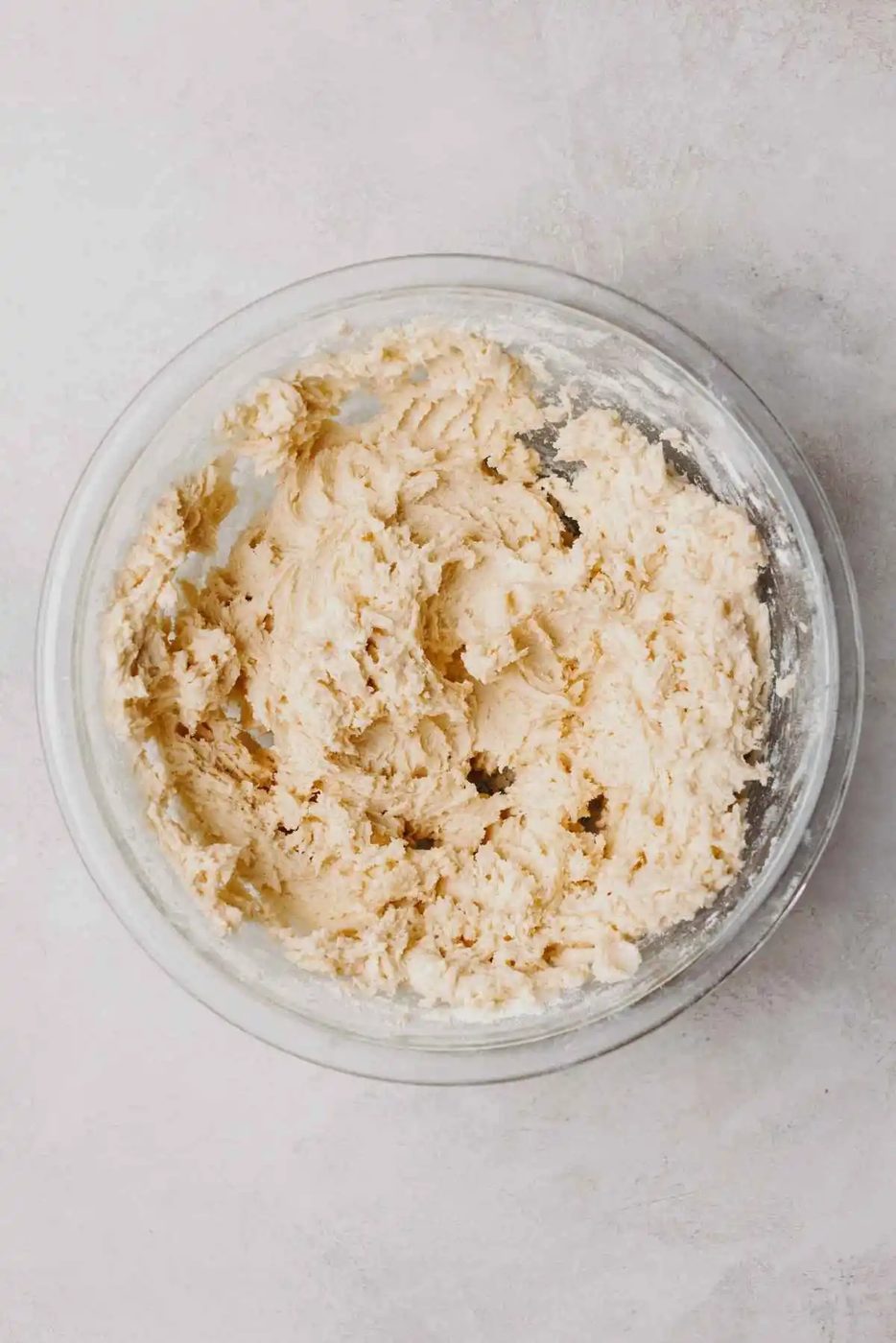 Almond cookie dough in a large glass mixing bowl on a light grey background.