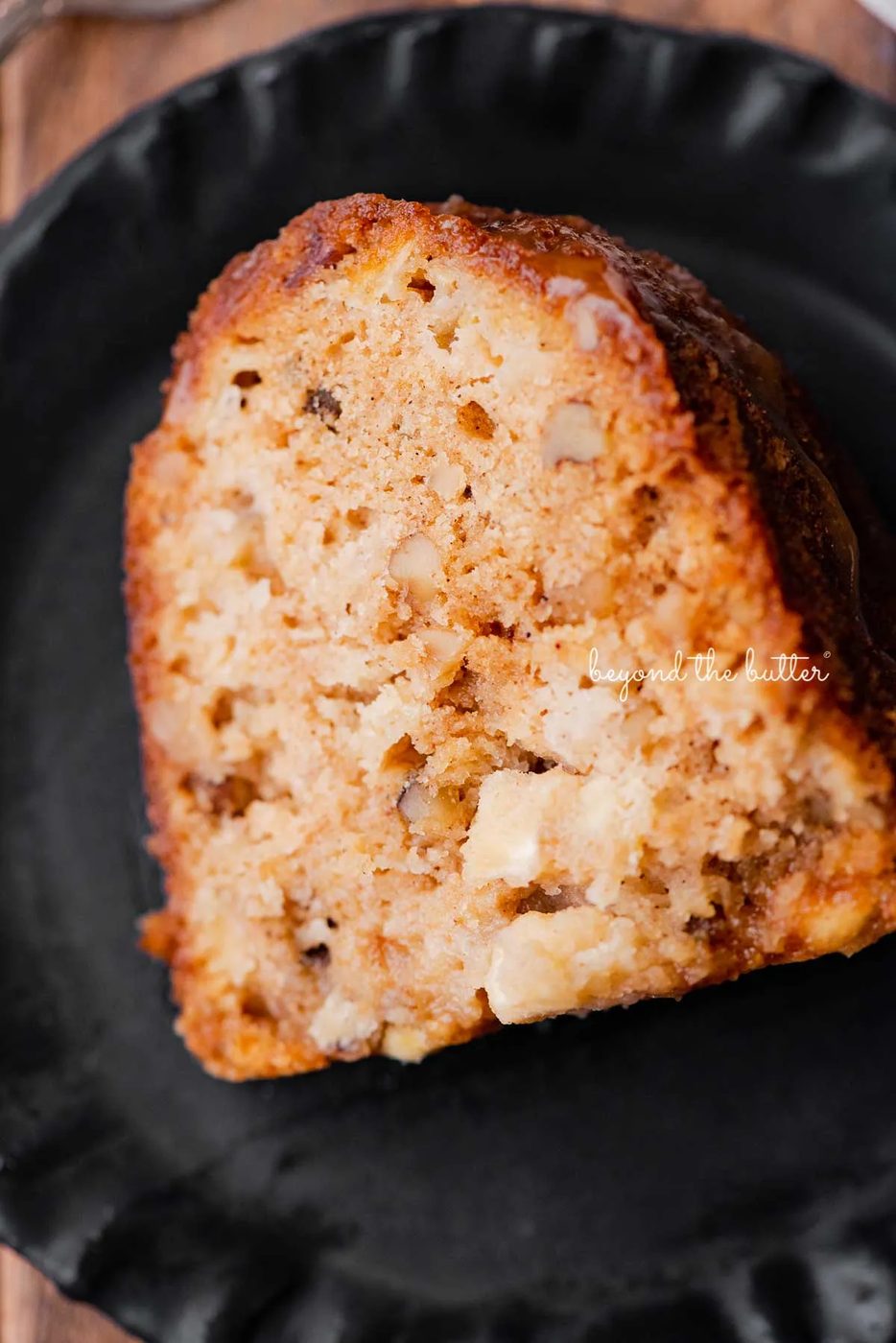 Slice of house-made apple bundt cake on dark wood background | © Sovuh