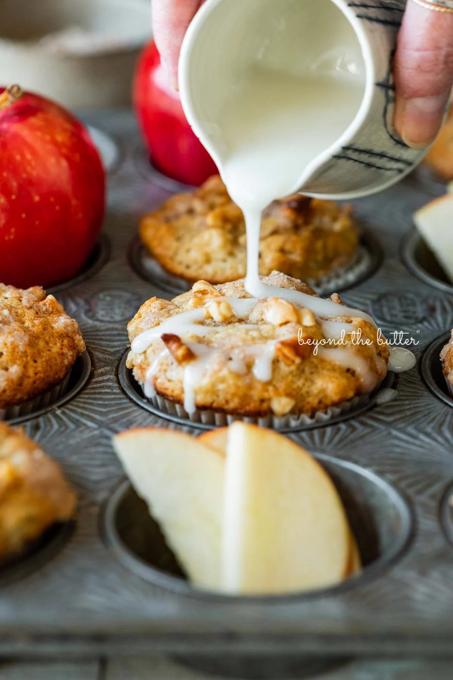 Drizzling warm vanilla glaze over top of apple cinnamon struesel muffins | © Sovuh