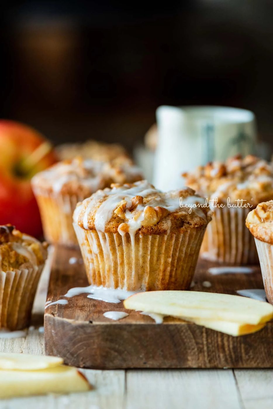 Warm apple cinnamon streusel muffins on a wood cutting board with slices of apples and vanilla glaze | © Sovuh