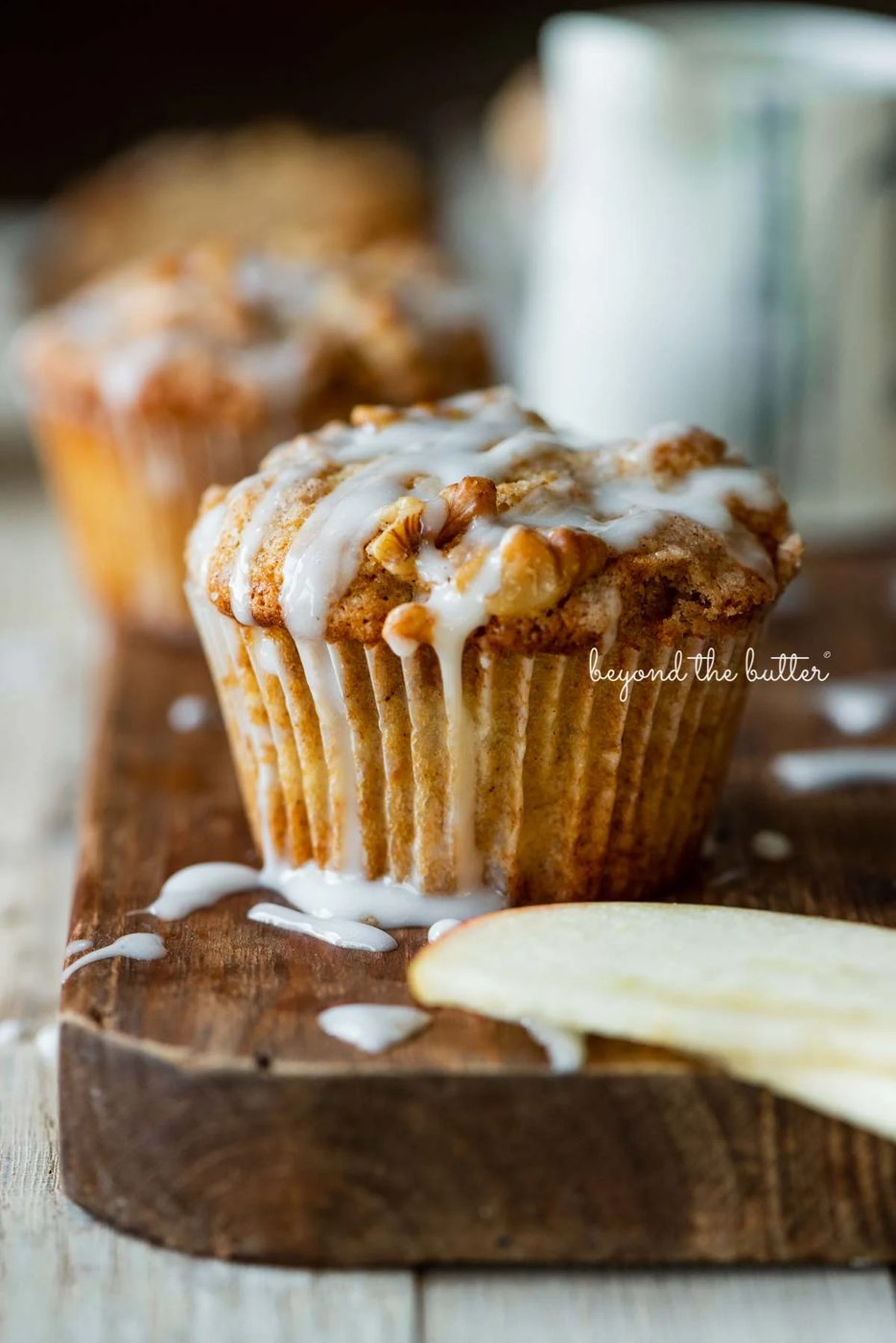 Warm apple cinnamon streusel muffins on a wood cutting board with slices of apples and vanilla glaze | © Sovuh