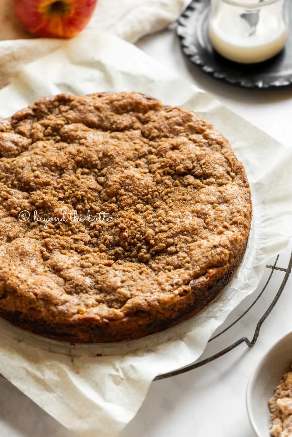 Cinnamon apple coffee cake colling on a parchment paper lined cooling rack with a glass of a simple vanilla glaze off to the side | All Images © Sovuh