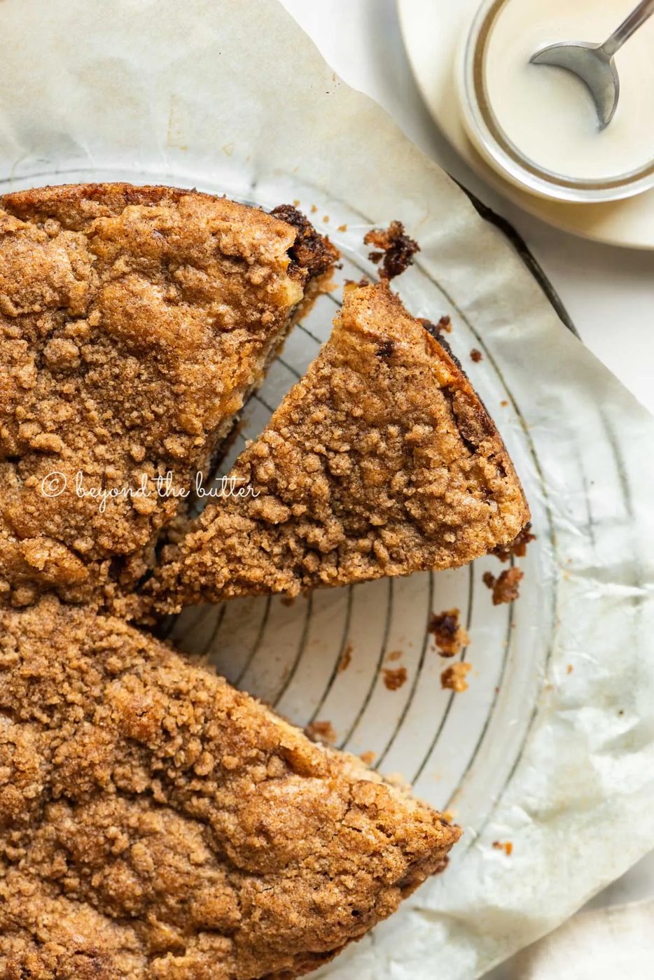 Apple coffee cake on a parchment paper lined wire cooling rack with slices removed and a simple vanilla glaze to the side | All Images © Sovuh