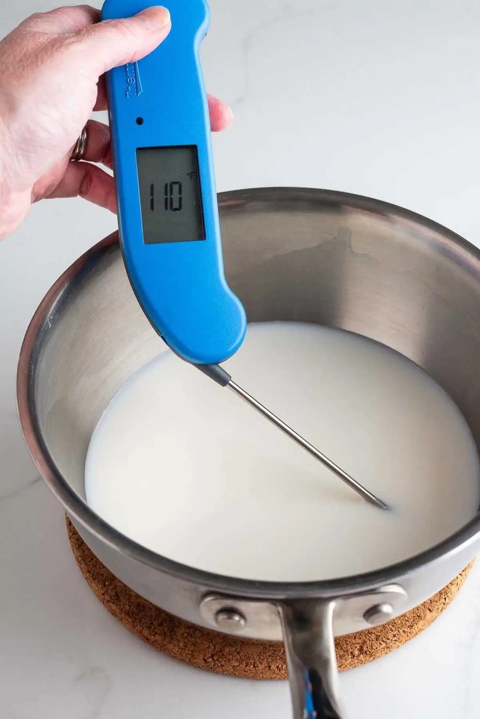Milk and water in saucepan warmed to 110 degrees fahrenheit using a blue digital thermometer.