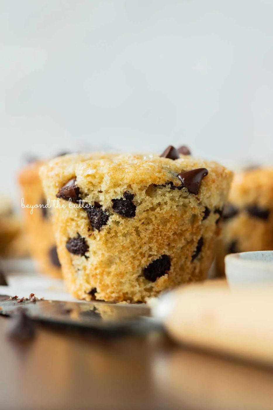 Single unwrapped bakery style chocolate chip muffin on a flattened muffin liner with white background | © Sovuh
