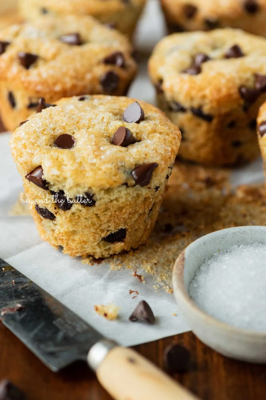 Bakery style chocolate chip mufins unwrapped with a small dipping bowl of sparkling sugar nearby | © Sovuh