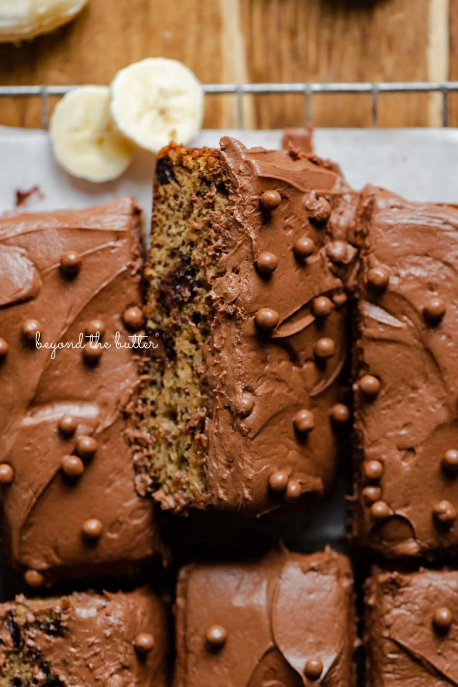 Slices of banana chocolate chip snack cake with chocolate cream cheese frosting on parchment paper lined cooling rack with banana slices | All images © Sovuh