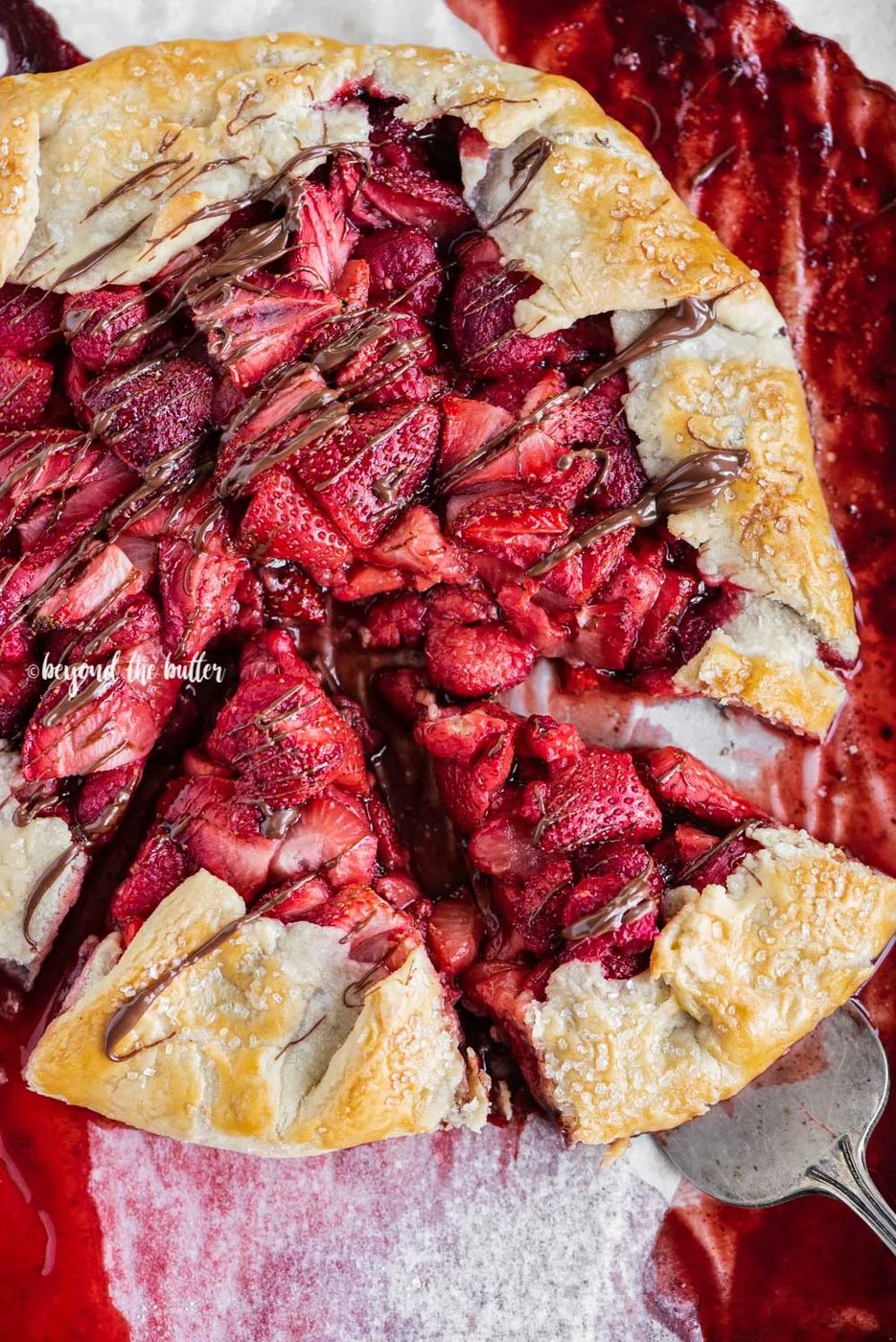 Overhead image of a Berry Nutella Galette on a baking sheet with Nutella drizzled over the top and 2 slices cut | All Images © Sovuh