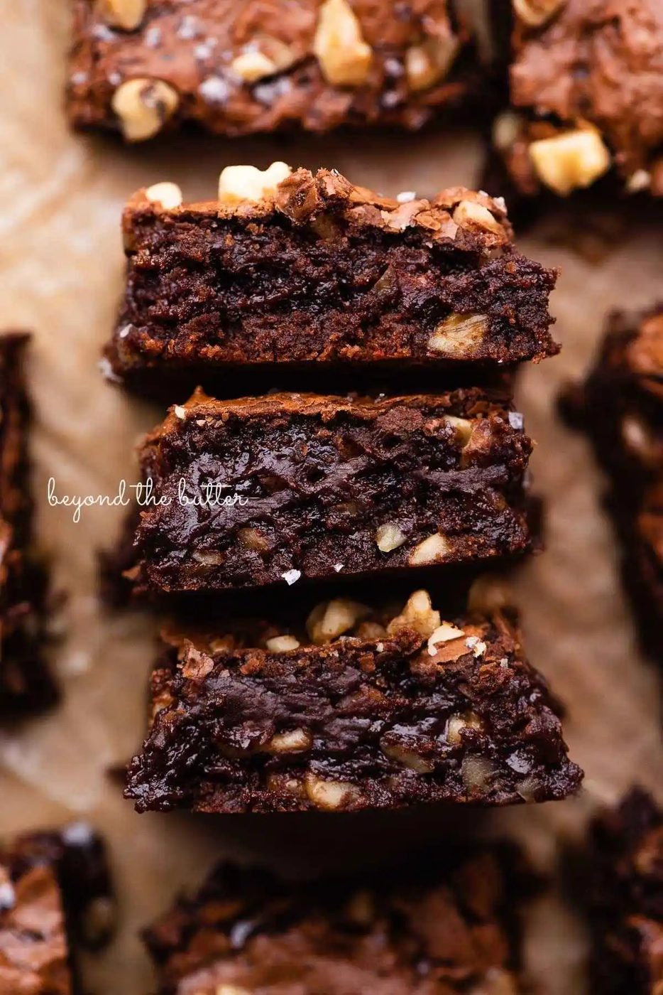 Three fudgy brownies on their side on brown parchment paper.