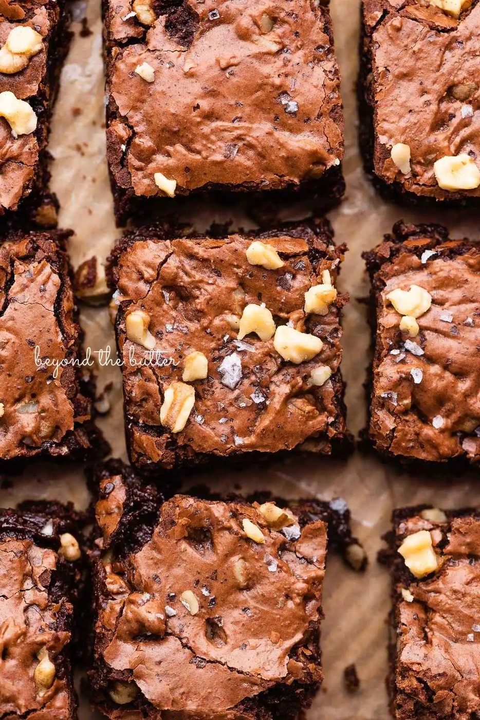Sliced fudgy brownies topped with chopped walnuts and sea salt flakes on brown parchment paper.