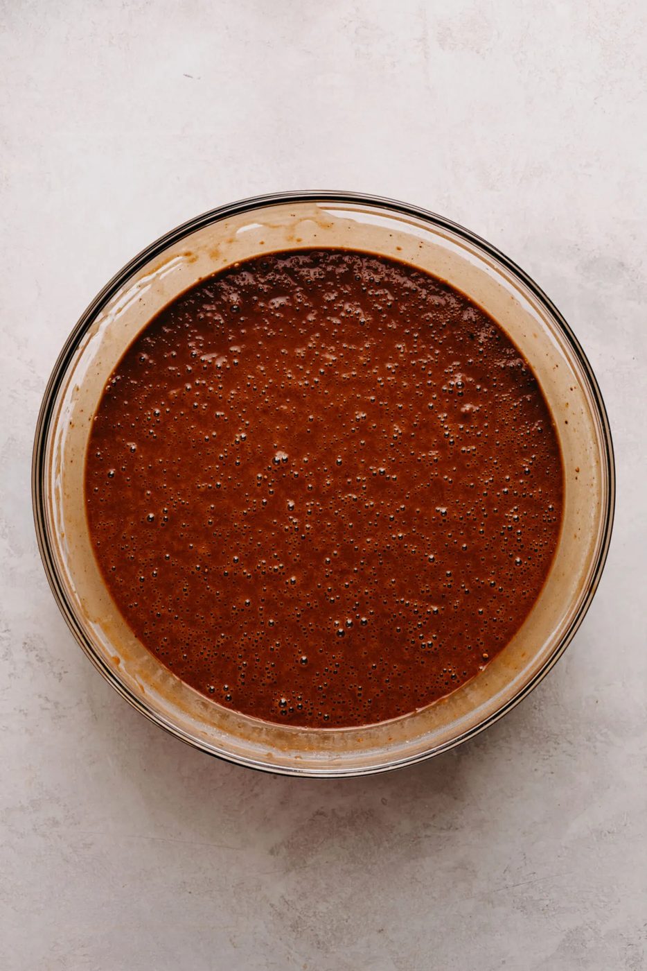 Black bottom cupcake batter mixed fully together in a large glass mixing bowl on a white marbled background.