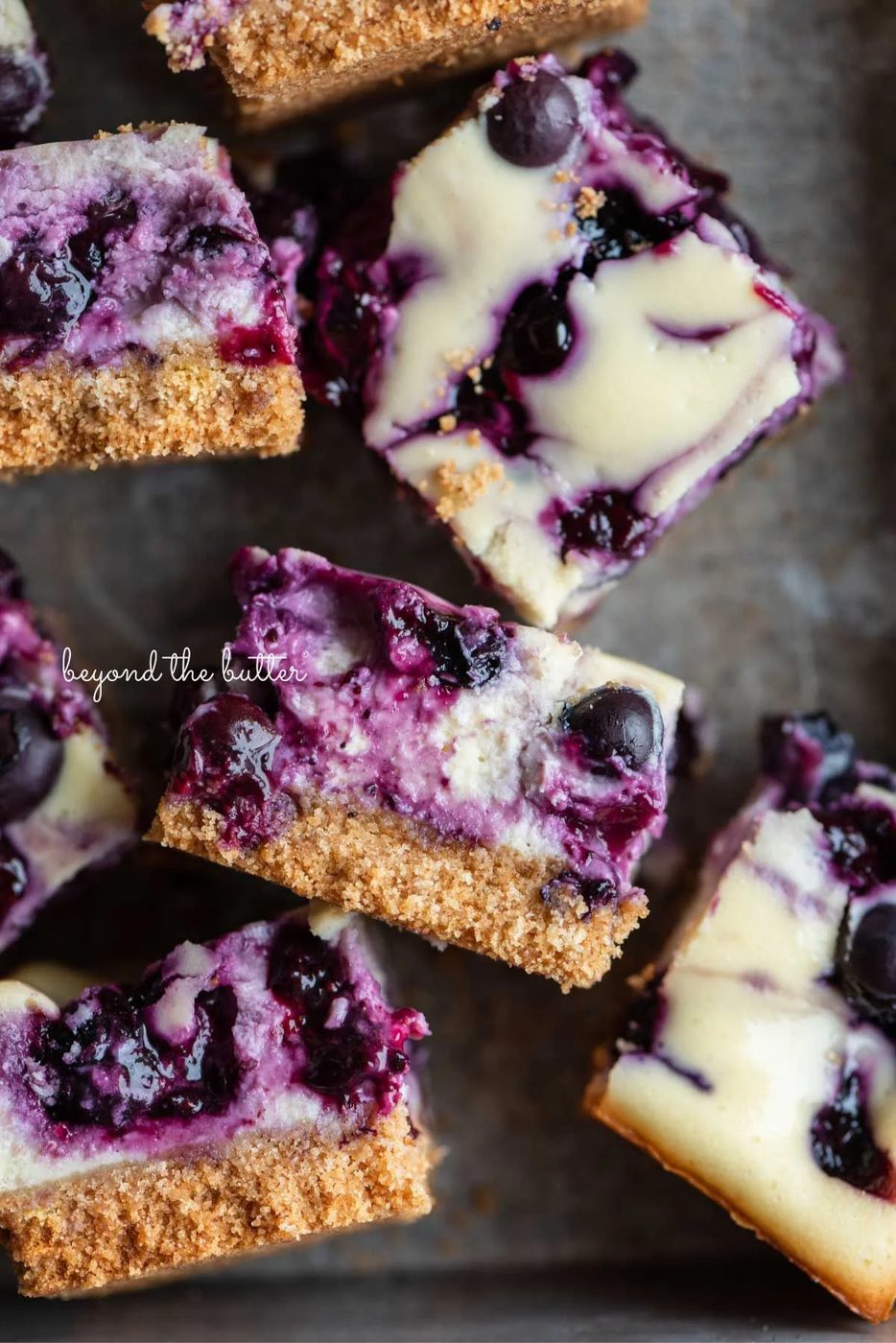 Sliced blueberry swirl cheesecake bars randomly placed in a vintage baking tin.