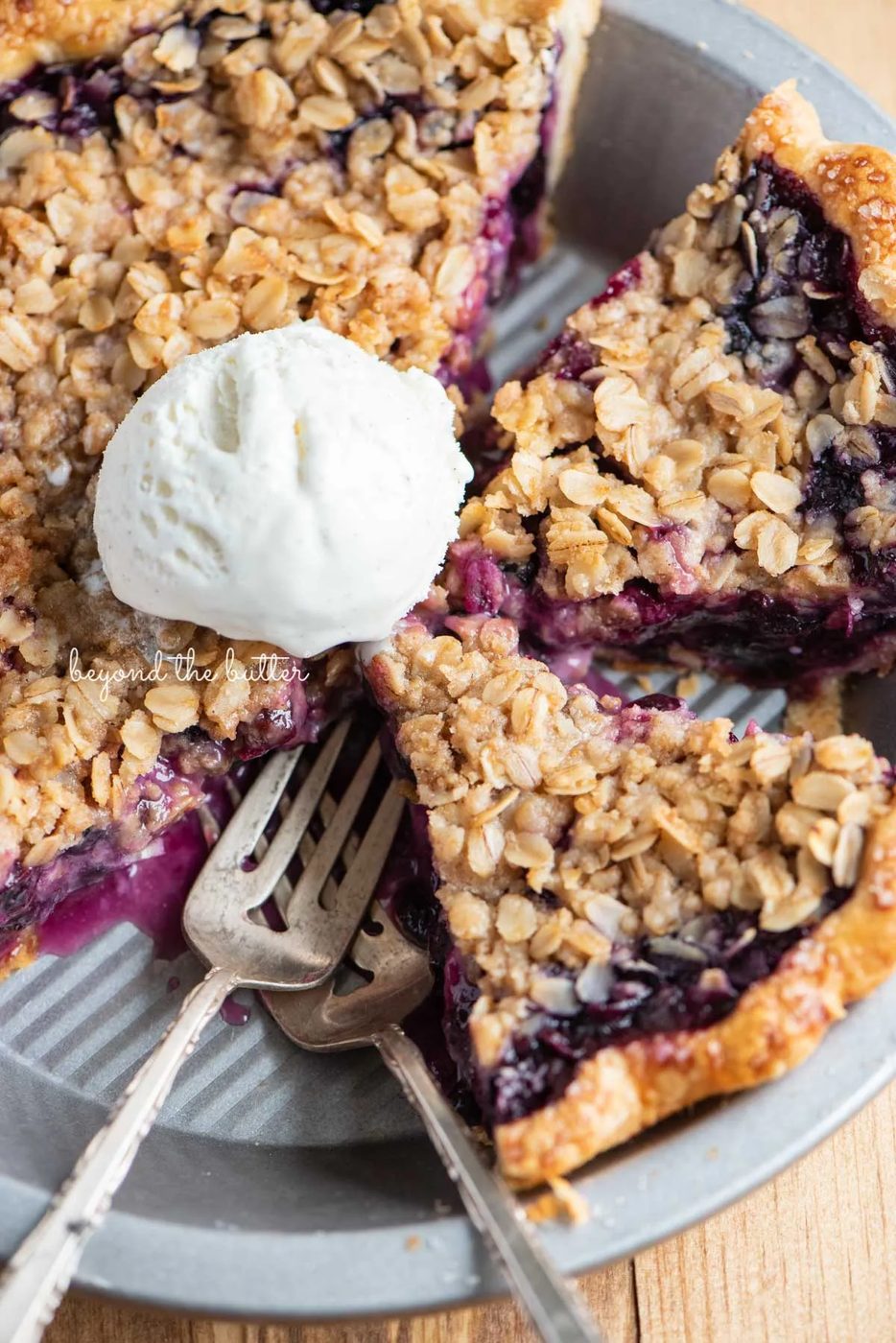 Slices of blueberry crumble pie in pie plate with scoopy of ice cream in the center | © Sovuh