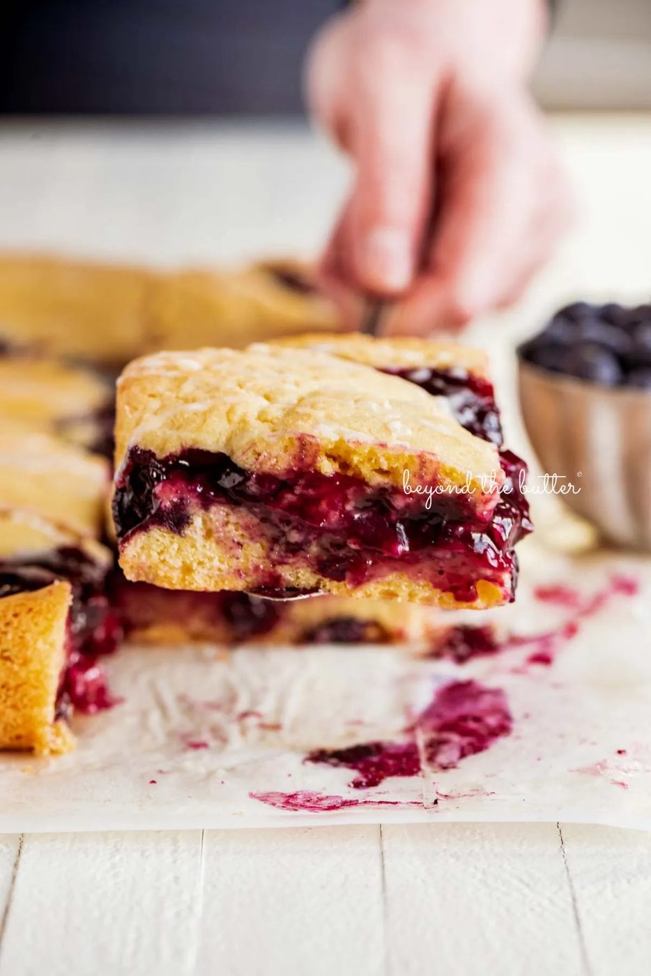 Serving a slice of freshly baked blueberry swirl coffee cake on wood table.