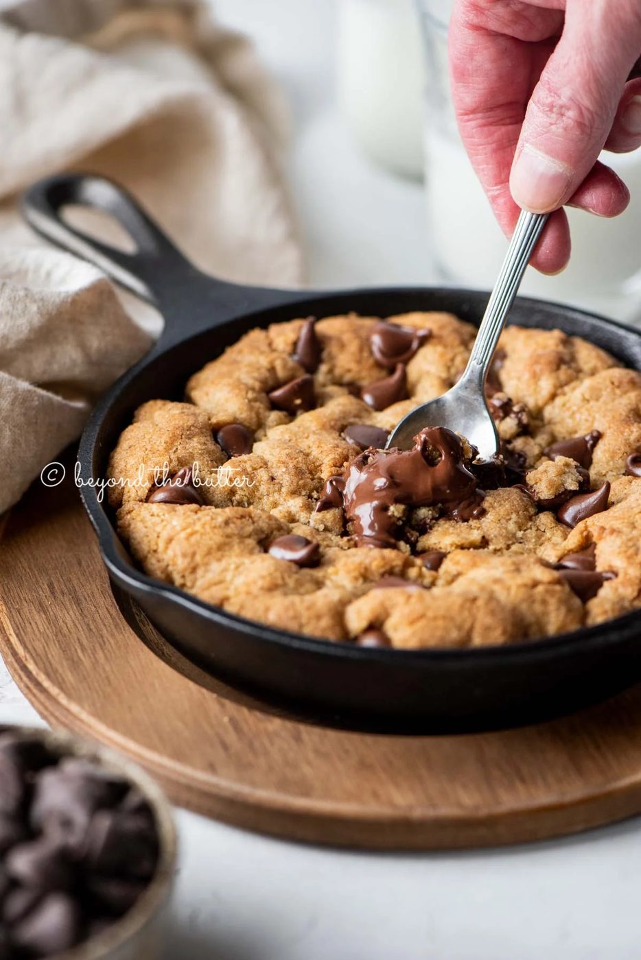 Warm brown butter chocolate chip skillet cookie with two spoons resting in skillet on wood trivet | All Images © Sovuh