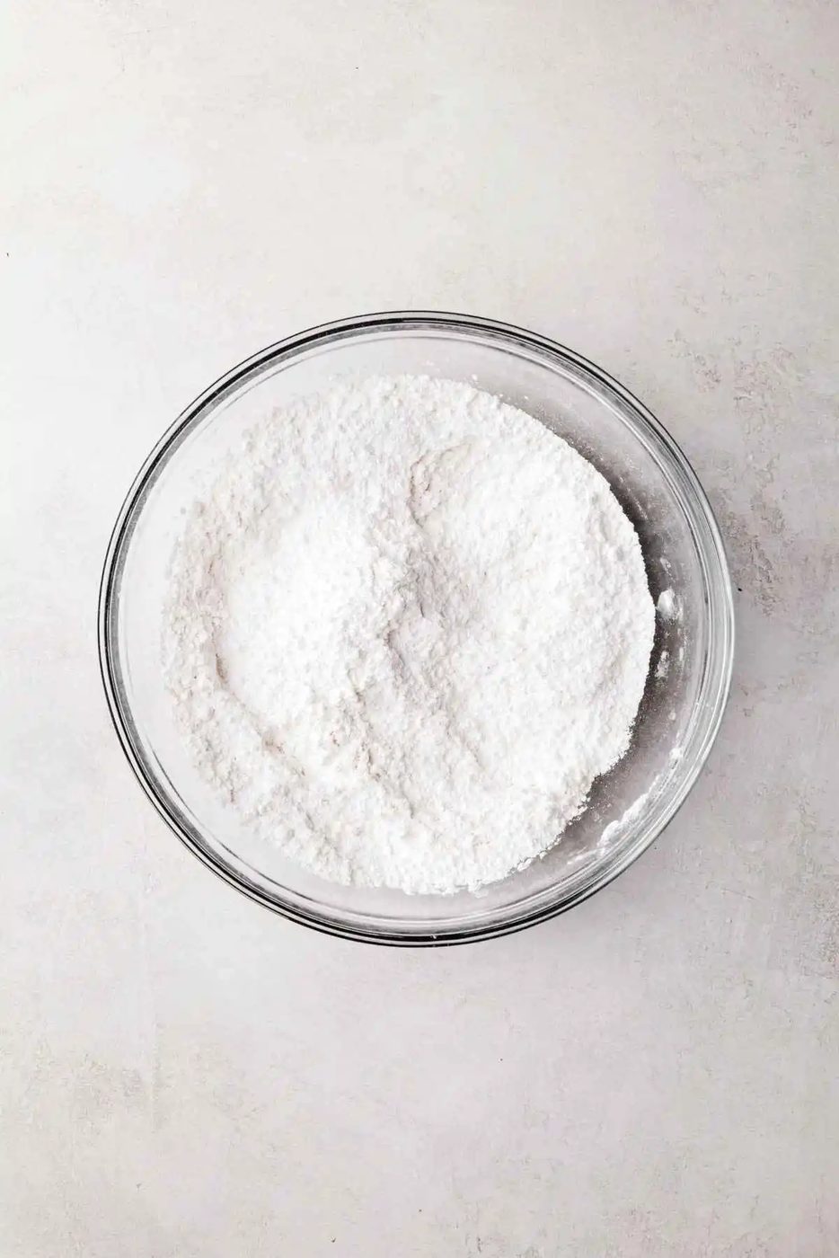 Whisked cake flour, baking powder, and salt in a small glass mixing bowl on a white and grey textured background.