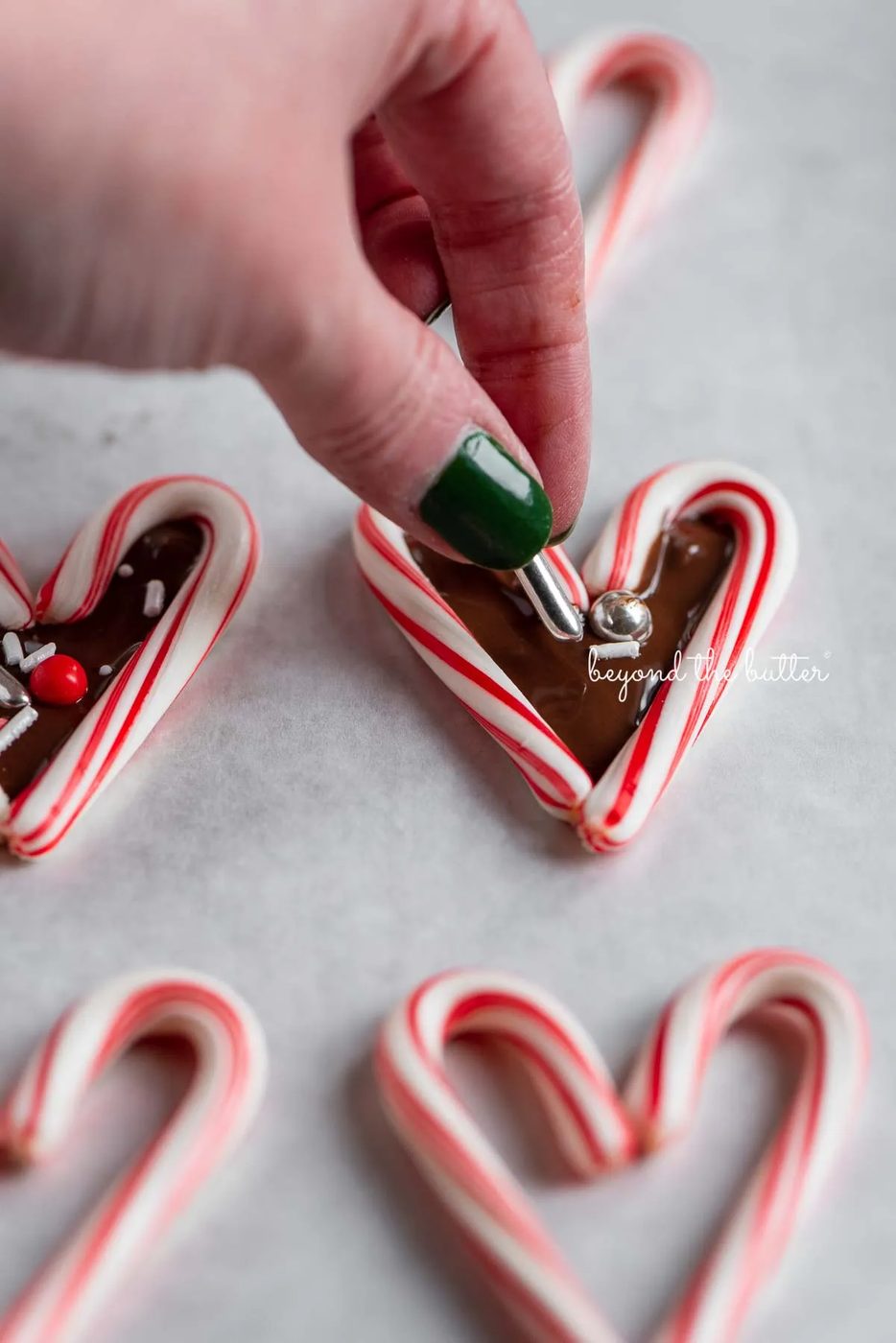 Adding holiday theme sprinkles to candy cane hearts filled with melted chocolate | © Sovuh