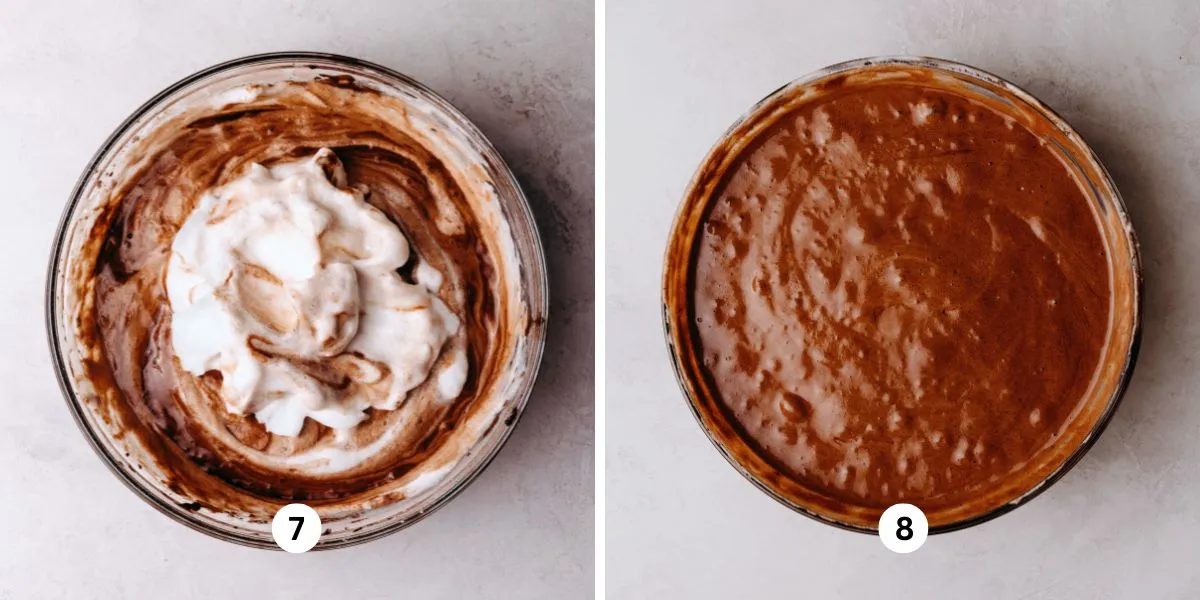 Folding meringue into chocolate chiffon cake batter in a large glass bowl on a white marbled background.