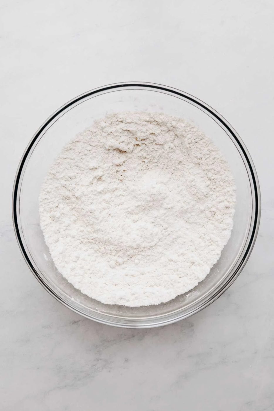 Whisked all purpose flour, baking powder, and salt in a large glass mixing bowl on a white and grey marbled background.