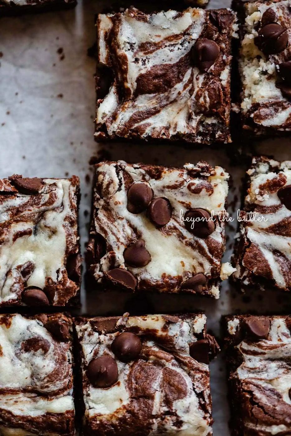 Sliced squares of chocolate chip cream cheese brownies on white parchment paper.