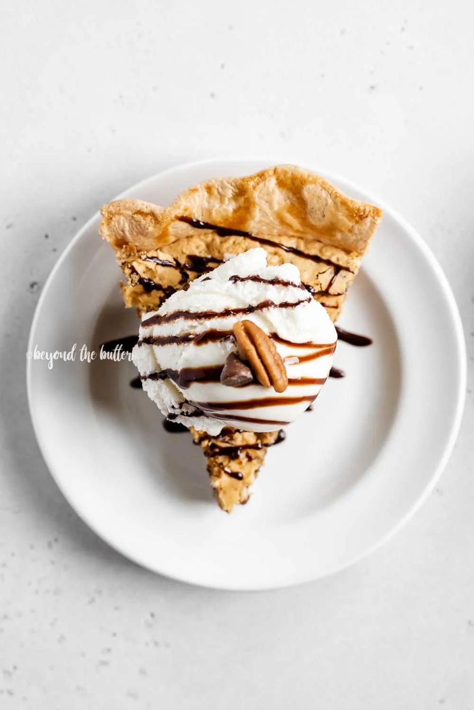 Overhead image of one slice of chocolate chip pie with a scoop of vanilla ice cream on top drizzled with chocolate syrup | All Images © Sovuh