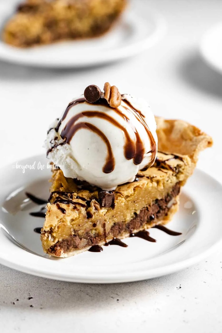 Angled closeup image of Chocolate Chip Pie with a scoop of vanilla ice cream on top that's drizzled with chocolate syrup | All Images © Sovuh