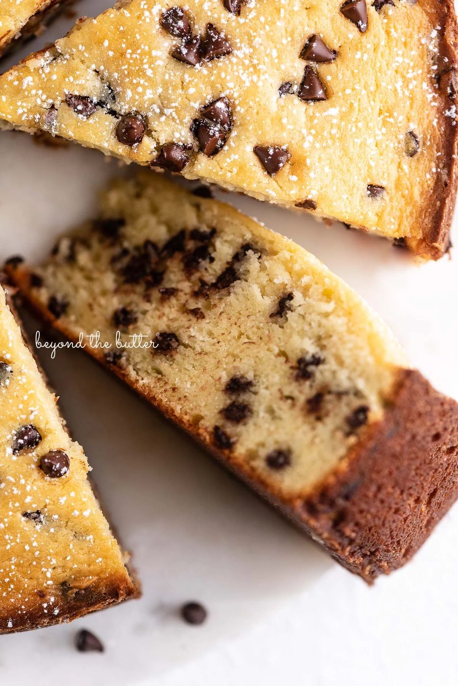 Slices of chocolate chip ricotta cake with one on its side on a marble cake round with small bowl of mini chocolate chips nearby | © Sovuh