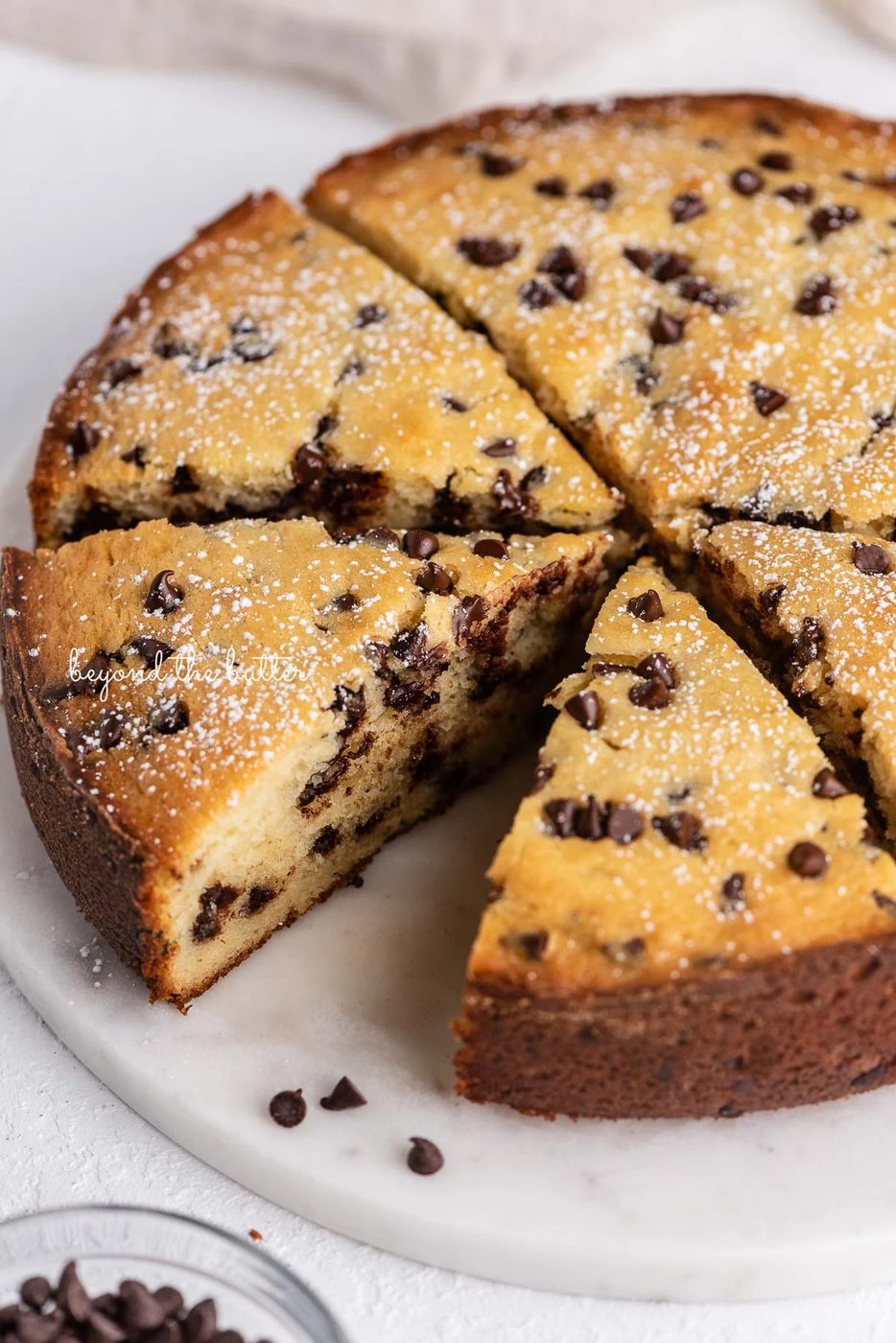Sliced chocolate chip ricotta cake on a marble cake round with small bowl of mini chocolate chips nearby | © Sovuh