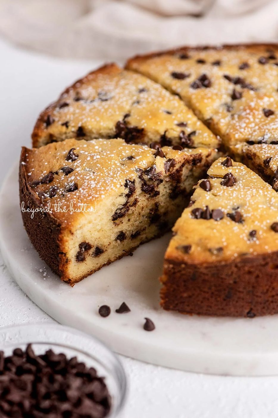 Slices of chocolate chip ricotta cake on a marble cake round with small bowl of mini chocolate chips nearby | © Sovuh