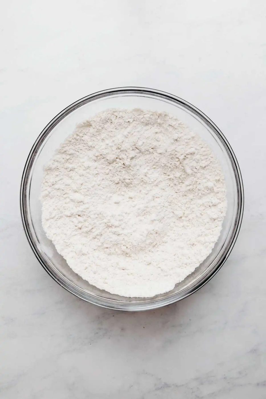 Whisked all purpose flour, baking powder, and salt in a large glass mixing bowl on a white and grey marbled background.