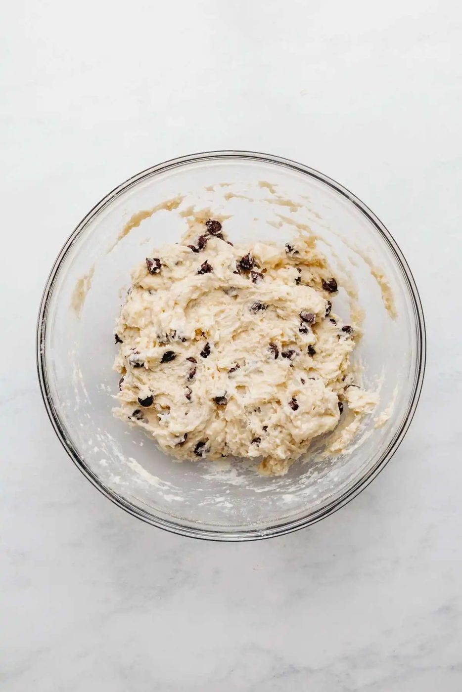 Chocolate chips mixed into scones mixture in a large glass mixing bowl on a white and grey marbled background.