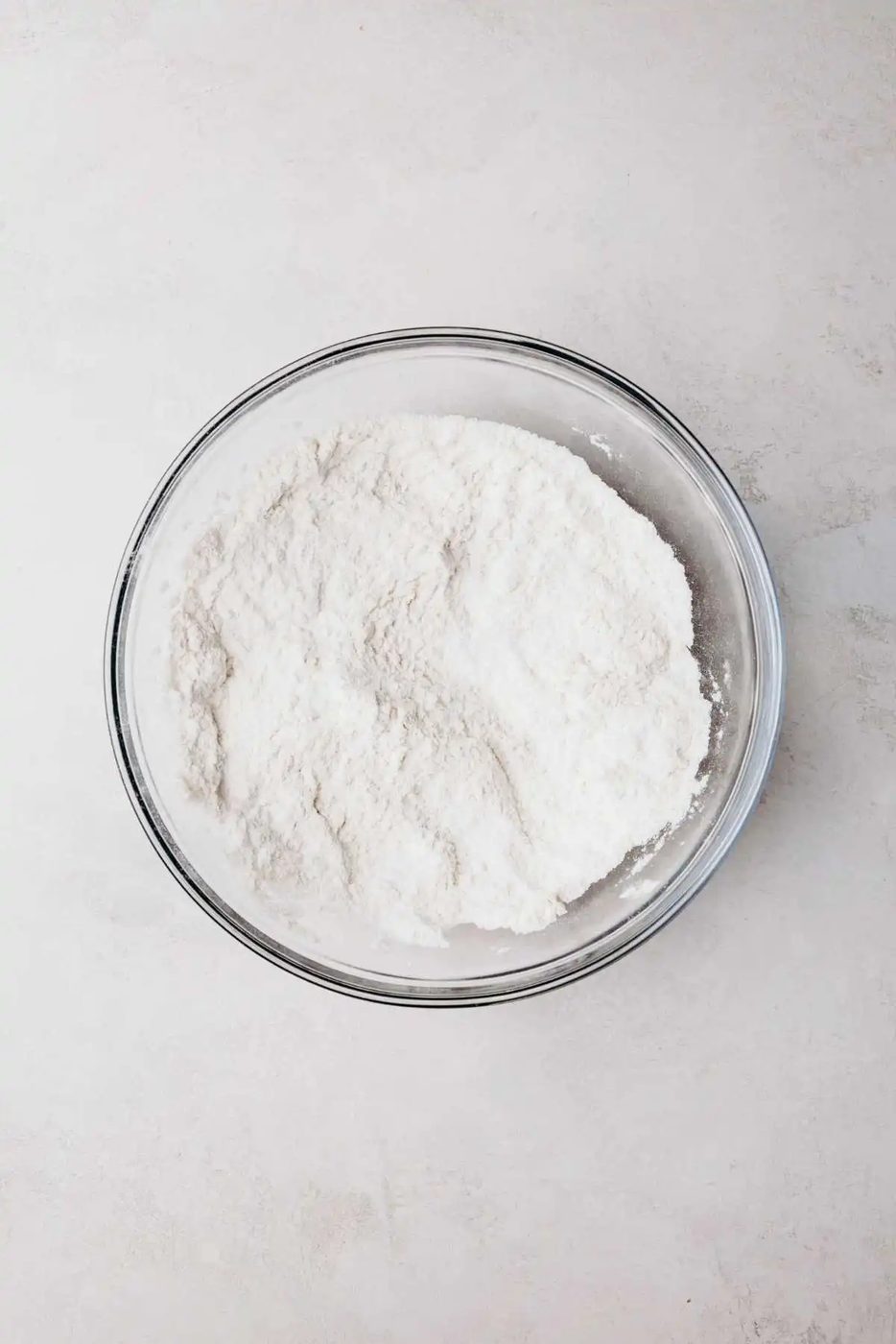 Whisked all purpose flour, baking powder, and salt in a small glass mixing bowl on a light grey background.