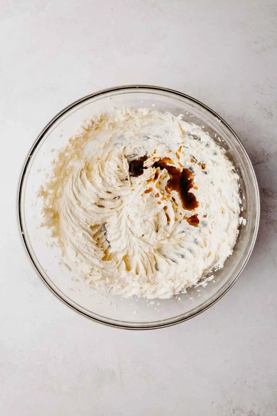 Unsalted butter, granulated sugar, and light brown sugar blended together in a large glass mixing bowl with vanilla extract added to the top for mixing.