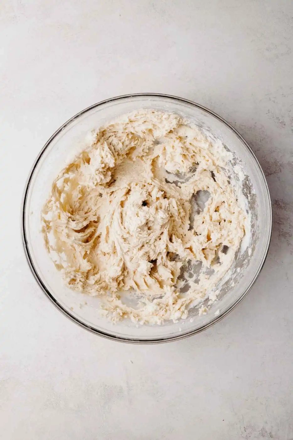 Shortbread cookie dough blended together in a large glass mixing bowl on a light grey background.