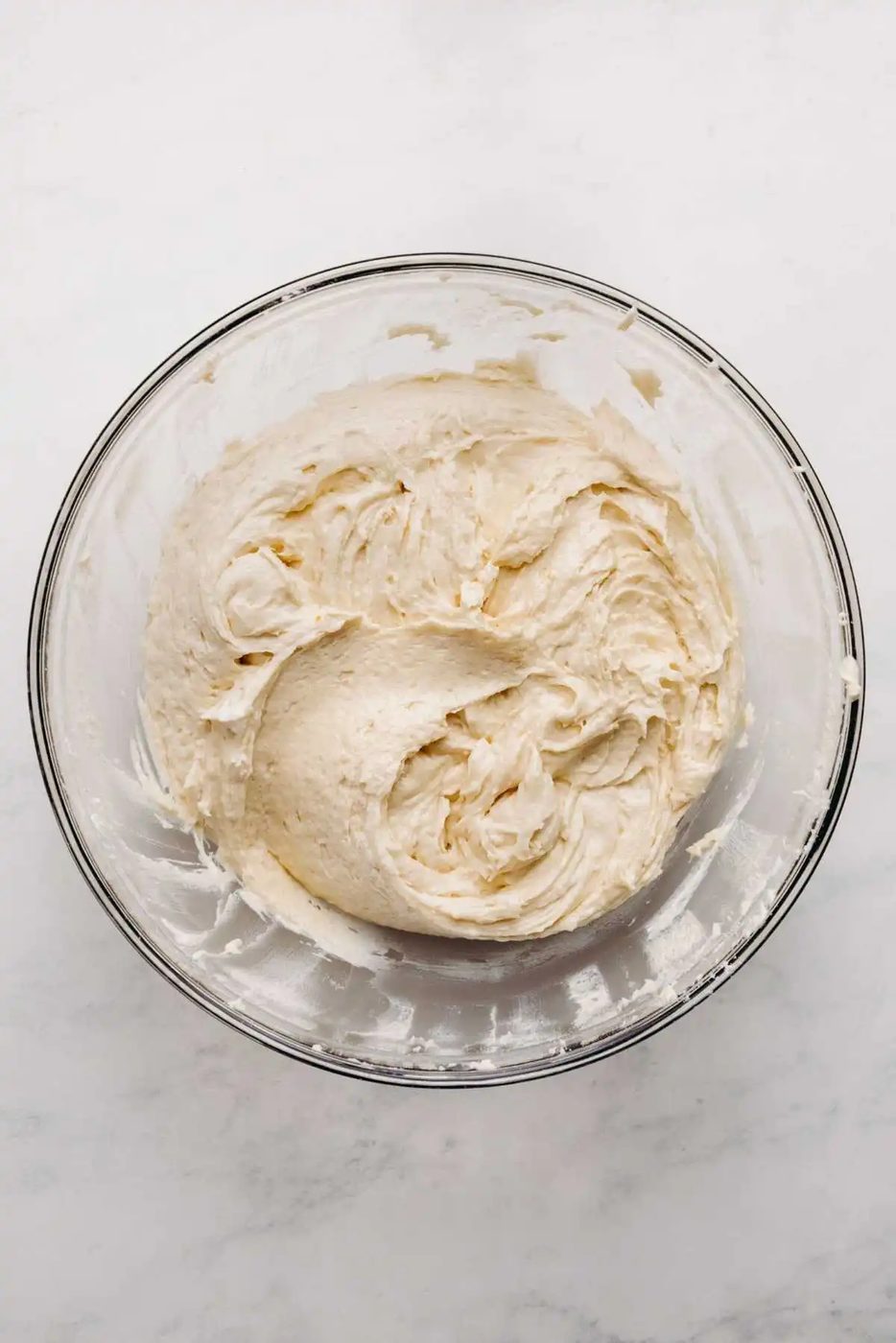 Sour cream coffee cake batter in a large glass mixing bowl on a white marbled background.