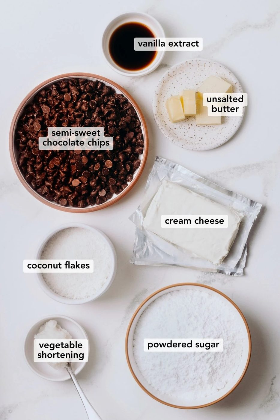 Chocolate covered coconut buttercream egg ingredients displayed in different size bowls on a white marble background.