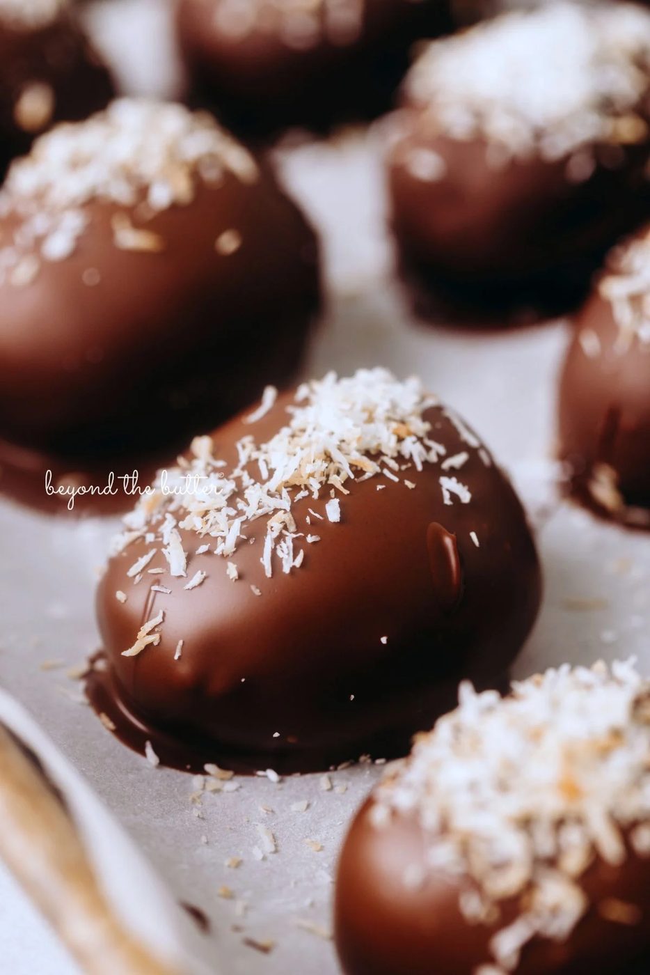 Chocolate covered coconut buttercream eggs topped with toasted coconut on a wax paper lined baking sheet.
