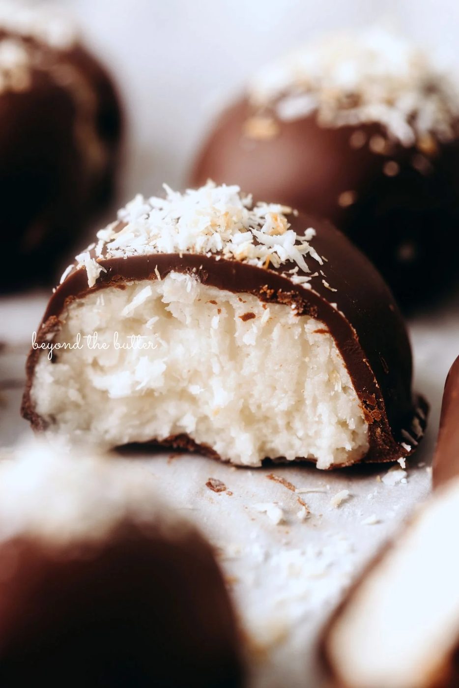 Chocolate dipped coconut buttercream eggs with center egg sliced in half to see the inside creamy texture on white background.