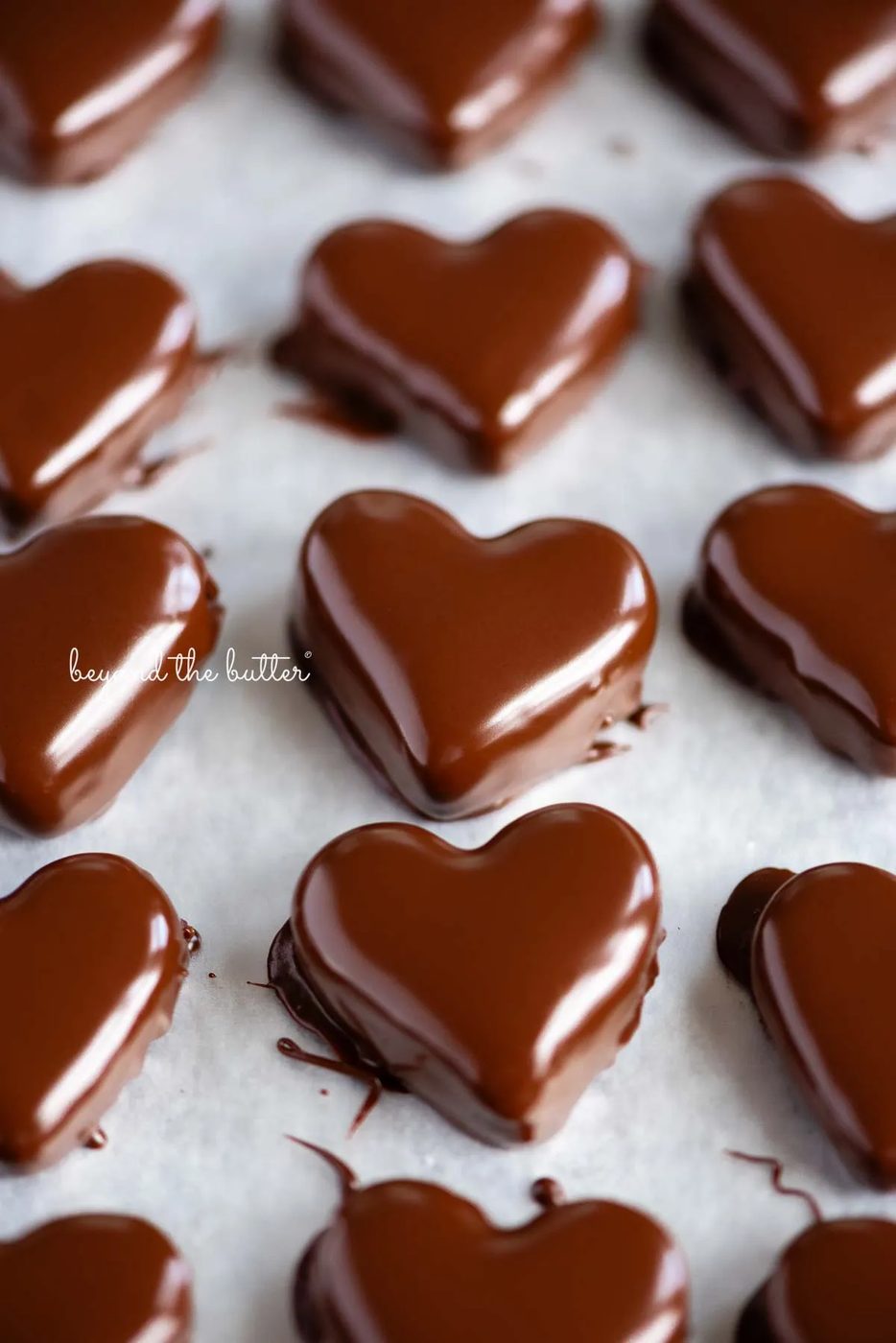 Rows of just dipped chocolate covered peanut butter hearts on a wax paper lined baking sheets.