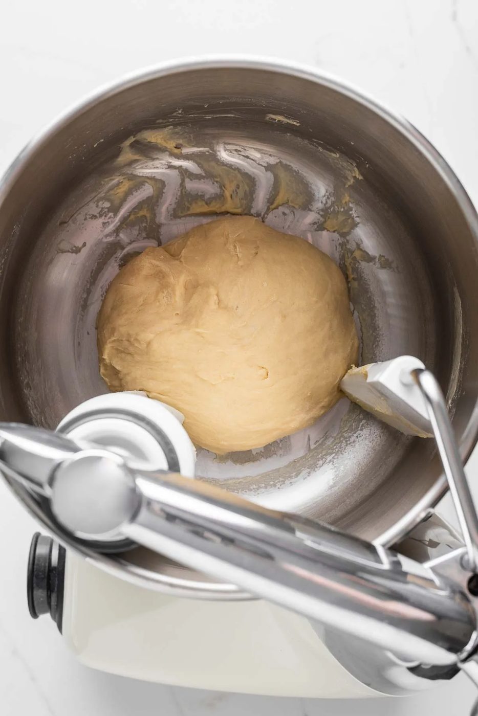 Mixing bread flour, warm milk, salt, an egg, melted unsalted butter, sugar, and yeast in an Ankasrum Assistent Original Mixer on a white marbled background.