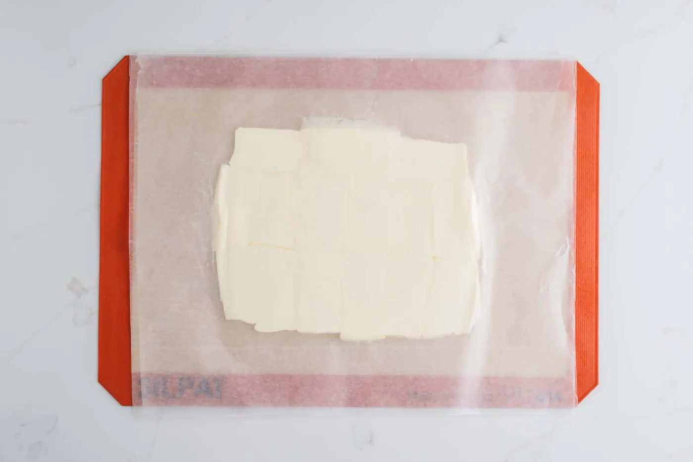 Rolled butter in a rectangular slab between two sheets of wax paper placed on a silicone baking sheet.