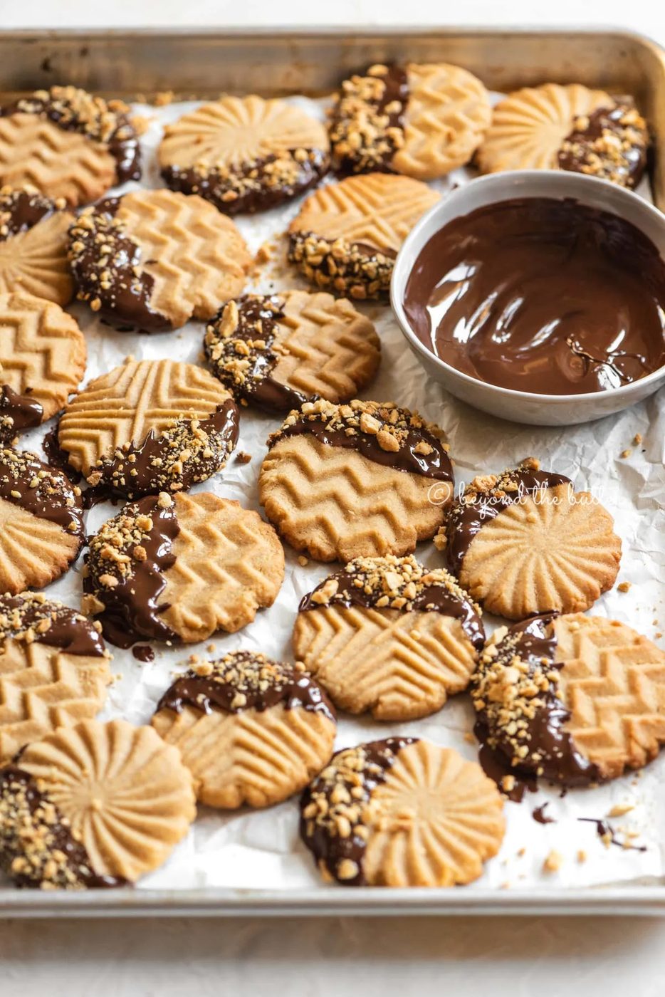 Baking sheet with randomly placed chocolate dipped peanut butter cookies with bowl of chocolate nearby | All Images © Sovuh