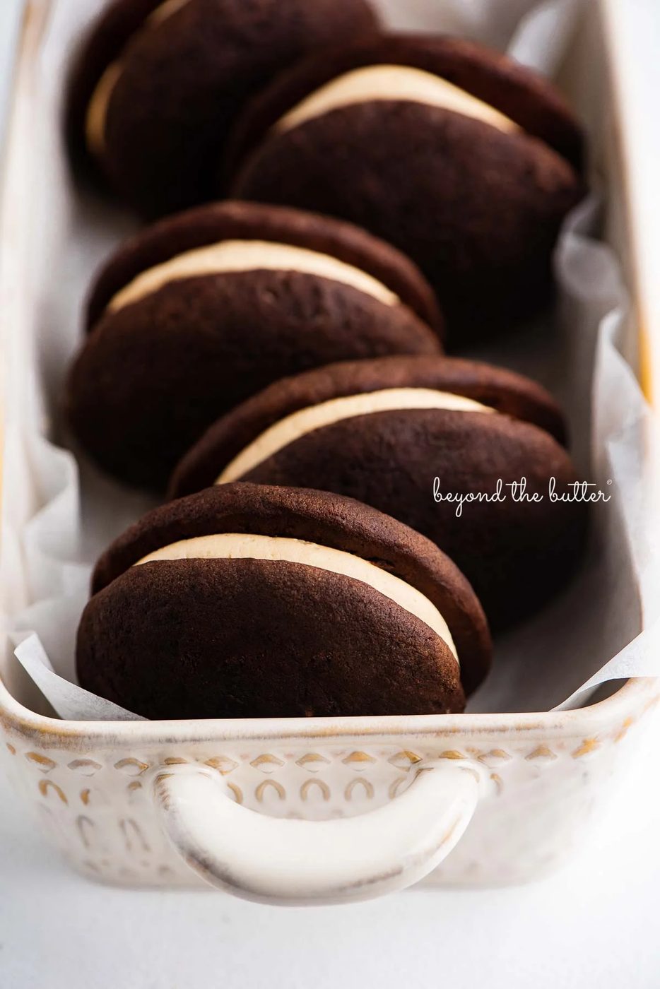 Ceramic loaf dish lined with parchment paper and chocolate peanut butter whoopie pies | © Sovuh