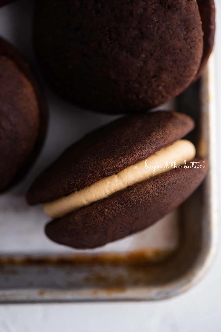 Closeup overhead image of chocolate peanut butter whoopie pies on a parchment lined baking pan | © Sovuh
