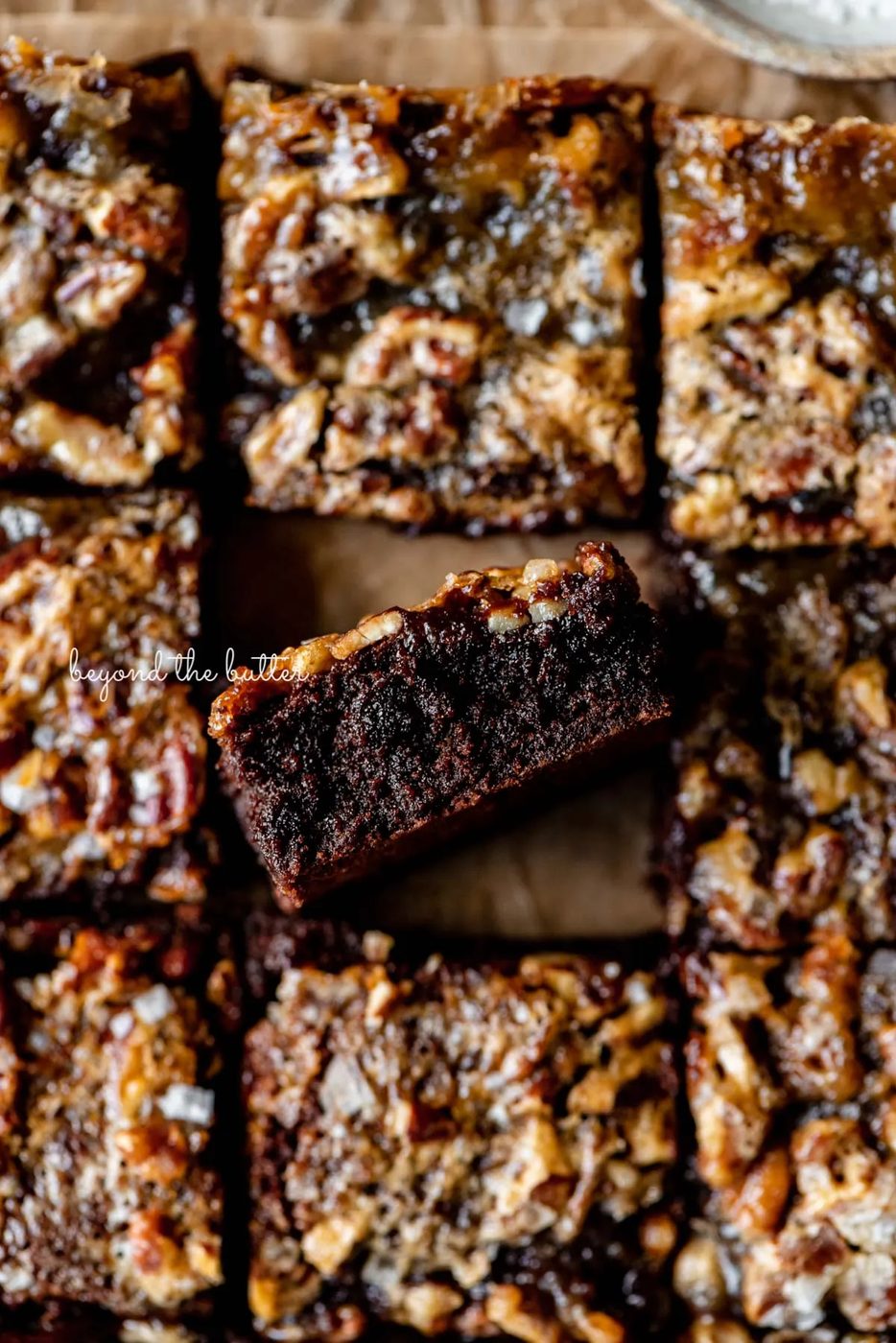 Salted pecan pie brownies placed on brown parchment paper with the center brownie placed on its side | © Sovuh