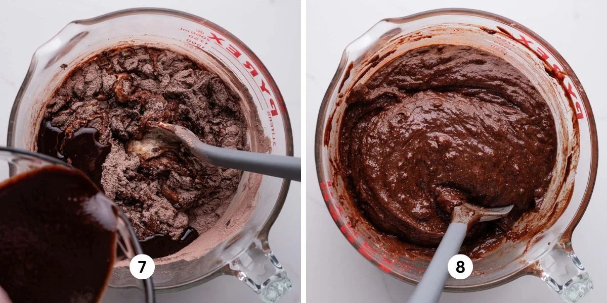 Stirring dry and wet ingredients together with a grey spatula in a glass mixing bowl on a white marbled background.