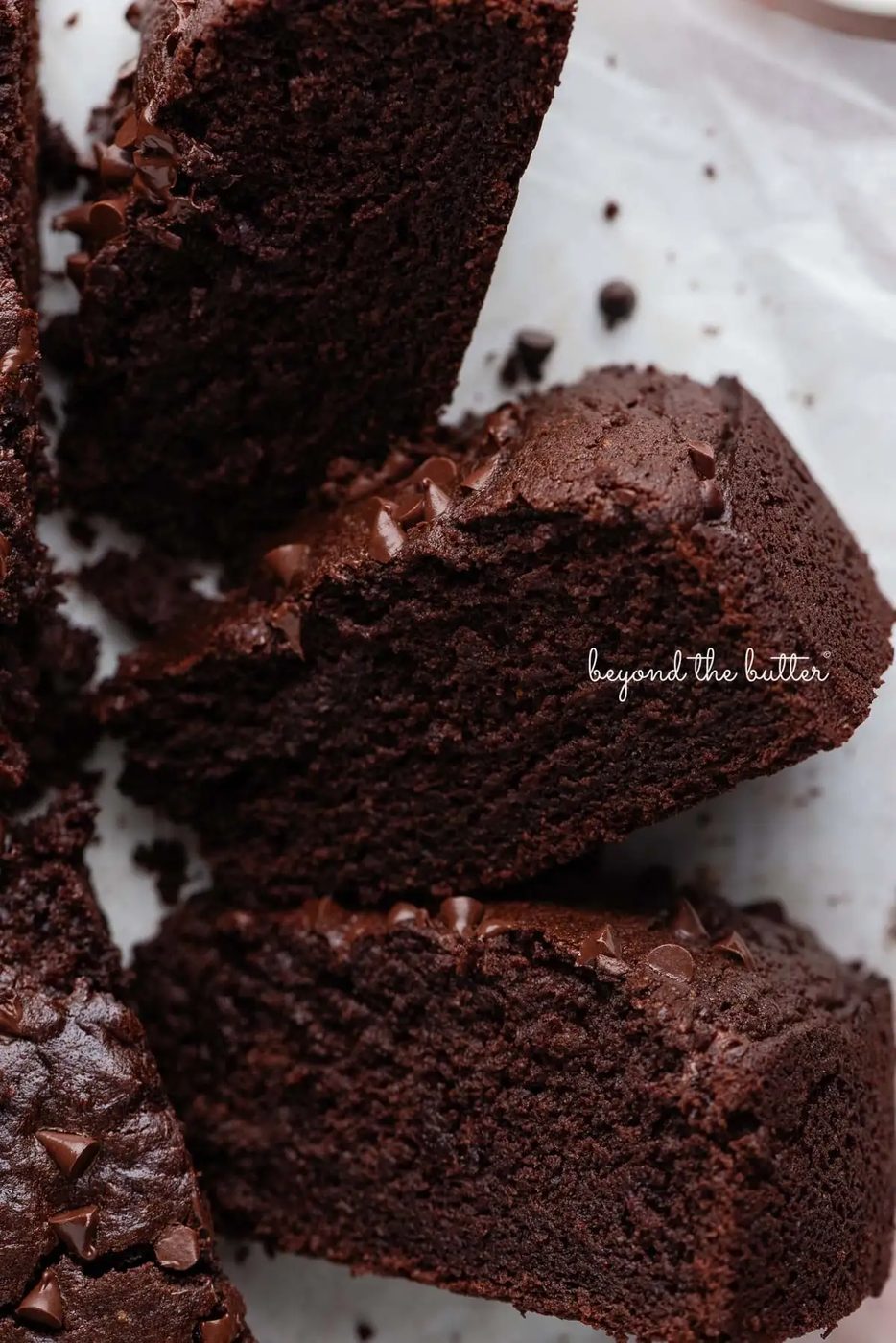 Slices of chocolate ricotta cake on their sides placed on white parchment paper and light pink background.